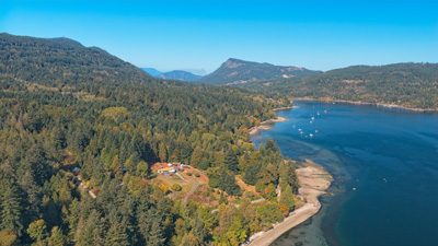 Aerial view of a Gulf Islands waterfront property with mountains and sailboats at anchor